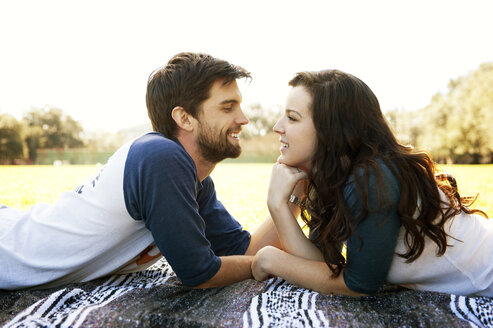 Seitenansicht eines romantischen Paares, das sich im Park liegend gegenseitig ansieht - CAVF00785