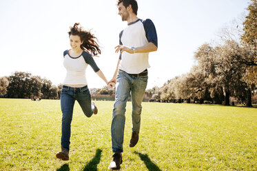 Couple running on grassy field at park during sunny day - CAVF00789