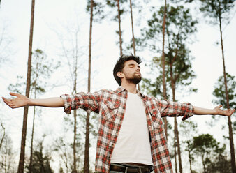 Man with arms outstretched standing against trees in forest - CAVF00791