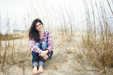 Portrait of happy woman sitting on sand at beach - CAVF00817