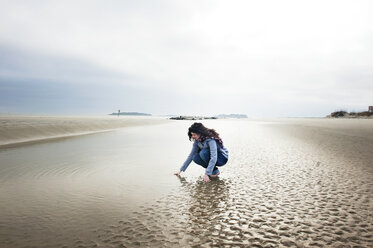 Woman crouching on beach against cloudy sky - CAVF00818