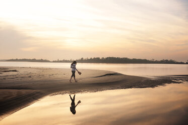 Woman walking on seashore against sky during sunset - CAVF00822