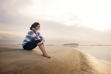 Thoughtful woman sitting on seashore against sky - CAVF00823