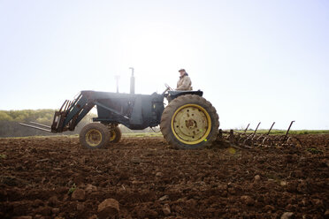 Landwirt fährt Traktor auf einem Feld gegen den klaren Himmel - CAVF00836