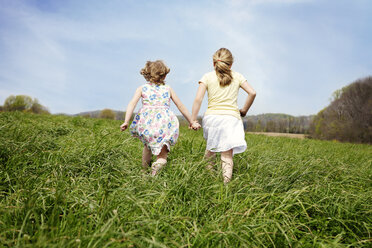 Rückansicht von Mädchen, die auf einem grasbewachsenen Feld gegen den Himmel laufen - CAVF00844