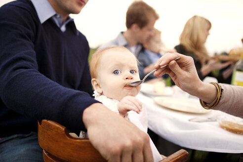 Ausgeschnittenes Bild einer Mutter, die ihr kleines Mädchen am Picknicktisch füttert - CAVF00851