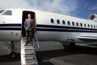 Businessman standing on steps of corporate jet - CAVF00865