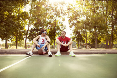 Freunde entspannen sich auf dem Basketballplatz vor den Bäumen im Park - CAVF00886