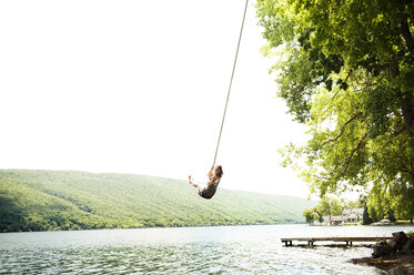 Woman swinging on rope over lake against clear sky - CAVF00887