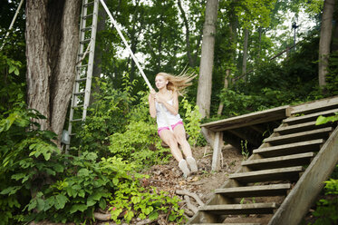 Junge Frau schwingt an einem Seil auf einer Treppe im Wald - CAVF00892