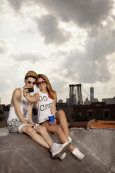 Happy young couple taking selfie on building terrace against cloudy sky - CAVF00904