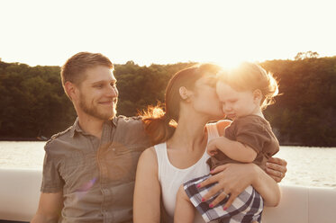 Woman kissing son while sitting with man in boat during sunset - CAVF00939