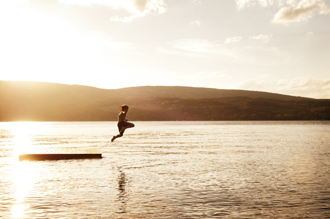 Junge taucht in den See gegen den Himmel bei Sonnenuntergang, lizenzfreies Stockfoto