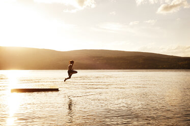 Boy diving into lake against sky during sunset - CAVF00977