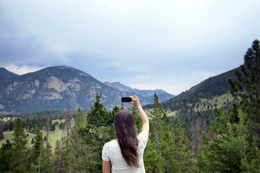 Rear view of woman photographing mountains with smart phone - CAVF00996