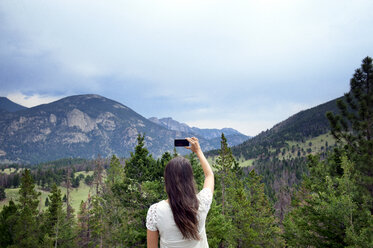 Rückansicht einer Frau, die mit ihrem Smartphone Berge fotografiert - CAVF00996