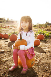 Portrait of cute girl sitting on pumpkin at field - CAVF01008