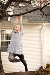 Low angle view of cheerful girl hanging from tree in yard - CAVF01018
