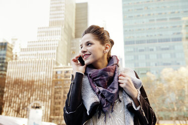 Low angle view of beautiful woman talking on mobile phone against buildings - CAVF01025