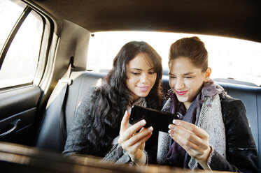 Glückliche Freundinnen, die während der Fahrt im Auto ihr Smartphone benutzen - CAVF01030