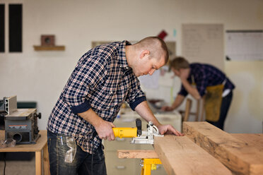 Männlicher Schreiner, der in einer Werkstatt Holz mit Geräten prüft - CAVF01035