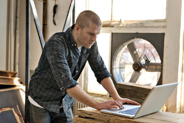 Side view of male carpenter using laptop in workshop - CAVF01043