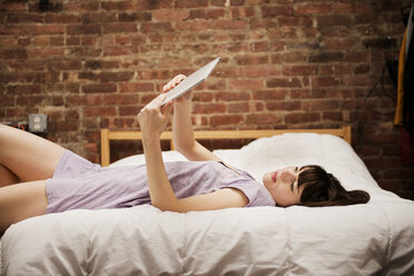 Junge Frau auf dem Bett liegend und mit digitalem Tablet zu Hause - CAVF01057