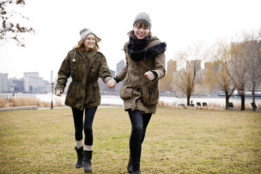 Smiling female friends holding hands and walking on grassy field - CAVF01062