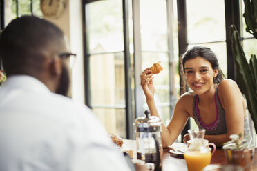 Portrait smiling young woman enjoying croissant and coffee in cafe - CAIF04609