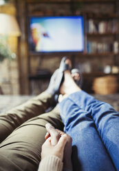 Personal perspective affectionate couple holding hands watching TV in living room - CAIF04610