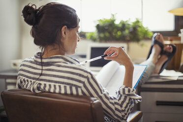 Businesswoman reading paperwork with feet up on desk - CAIF04612