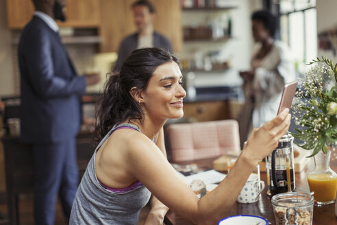 Junge Frau schreibt am Frühstückstisch eine SMS mit ihrem Smartphone - CAIF04619