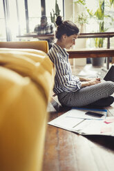 Female freelancer working at laptop on living room floor - CAIF04625