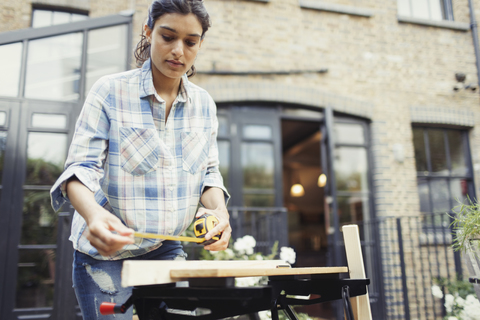 Junge Frau mit Maßband misst Holz auf der Veranda, lizenzfreies Stockfoto