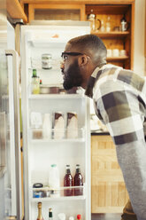 Junger Mann blickt in den Kühlschrank - CAIF04630
