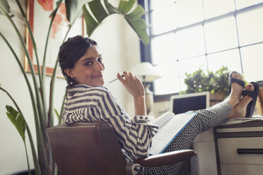 Portrait confident businesswoman working, reviewing paperwork with feet up on desk - CAIF04631