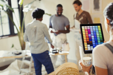 Junge Frau mit digitalem Tablet, die digitale Farben betrachtet, malt im Wohnzimmer - CAIF04633