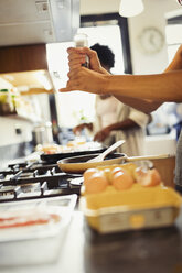 Frau knackt frischen Pfeffer auf Eier kochen auf dem Herd in der Küche - CAIF04634