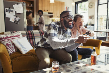 Männliche Freunde trinken Bier und spielen ein Videospiel im Wohnzimmer - CAIF04639