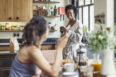 Lächelndes lesbisches Paar, das Kaffee und Frühstück in der Küche genießt - CAIF04648