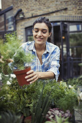 Young woman gardening, holding potted plant on patio - CAIF04659
