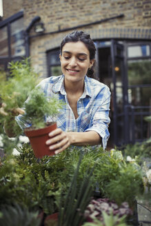 Junge Frau bei der Gartenarbeit, hält Topfpflanze auf der Veranda - CAIF04659