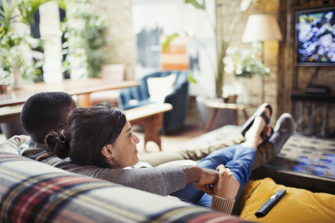 Zärtliches junges Paar beim Fernsehen auf dem Wohnzimmersofa, lizenzfreies Stockfoto