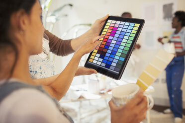 Junge Frau trinkt Kaffee und betrachtet digitale Farbmuster auf einem digitalen Tablet - CAIF04668