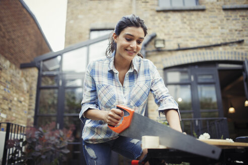 Young woman with saw cutting wood on patio - CAIF04676