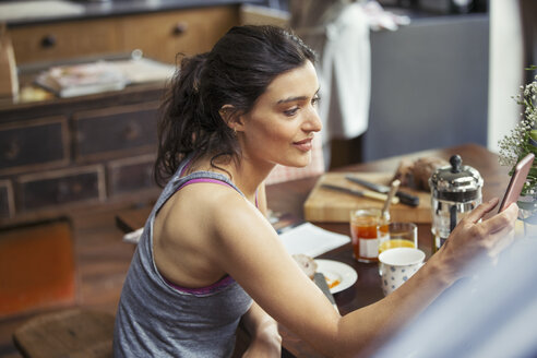 Junge Frau schreibt am Frühstückstisch eine SMS mit ihrem Smartphone - CAIF04678