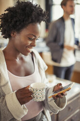 Lächelnde Frau trinkt Kaffee und schreibt eine SMS mit ihrem Smartphone - CAIF04702
