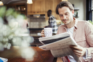 Man drinking coffee and reading newspaper in kitchen - CAIF04712