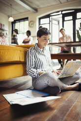 Female freelancer working at laptop on living room floor - CAIF04715