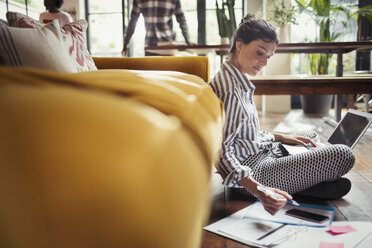 Female freelancer working at laptop on living room floor - CAIF04716